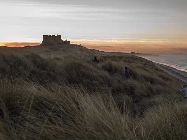 Children run through the sand dunes as the sun sets behind Bamburgh Castle